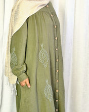 Load image into Gallery viewer, Side close up of khaki buttoned dress with embroidery detail on arm and bodice on a white curtain background