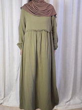 Load image into Gallery viewer, Woman wearing green pleated dress with light brown hijab in front of a white curtain.
