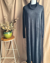 Load image into Gallery viewer, A charcoal grey long-sleeve cowl neck dress displayed on a mannequin, set against a beige fabric backdrop with a small wooden stool holding a green vase of dried flowers on the left.