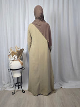 Load image into Gallery viewer, Side view of woman wearing beige modest cotton muslin maxi dress with flowing silhouette and long sleeves, standing against a white curtain, with a large ornamental vase with dried flowers next to her.