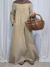 Load image into Gallery viewer, Woman wearing beige modest cotton muslin maxi dress with flowing silhouette and long sleeves, standing against a white curtain, with a basket in her hand.