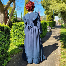 Load image into Gallery viewer, ginger-long-sleeve-embroidered-maxi-dress-with-ruffled-trim-over-shoulders-cinched-waistline-with-sash-tie-and-ruffled-hem-in-teal-next-to-garden-hedge-back-view