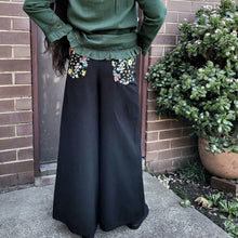 Load image into Gallery viewer, Luna high-waisted, wide leg, brushed cotton, women's pants in black, back view showing floral detail on back pockets, worn with green tunic