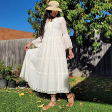 Load image into Gallery viewer, Sharon_tiered_midi_dress_in_cream_with_Vneckline_fitted_buttoned_bust_tiered_skirt_with_lace_trim_at_hem_and_bell_sleeves_with_lace_trim_front_of_garden_tree