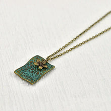 Load image into Gallery viewer, vintage-style-bronze-rectangle-pendant-necklace-with-verdigris-patina-finish-and-small-flower-charm-on-flat-surface