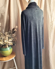 Load image into Gallery viewer, Back view of a charcoal grey long-sleeve long-sleeve cowl-neck dress displayed on a mannequin, set against a beige fabric backdrop with a small wooden stool and green vase of dried flowers on the left.
