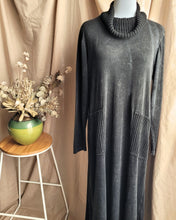 Load image into Gallery viewer, A charcoal grey long-sleeve maxi dress with a ribbed knit cowl neck and two large ribbed knit patch pockets, displayed on a mannequin against a beige fabric backdrop next to a small wooden stool with dried flowers.
