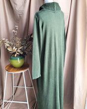 Load image into Gallery viewer, Back detail of khaki green long-sleeve cowl neck dress displayed on a mannequin torso, set against a backdrop of draped beige fabric. A small wooden stool with a green ceramic vase of dried flowers is positioned to the left.
