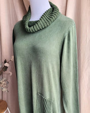 Load image into Gallery viewer, Close up of a khaki green knit dress showing ribbed cowl neck detail and a matching ribbed pocket, displayed on a white mannequin torso against a soft beige curtain backdrop.
