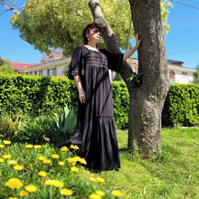 Load image into Gallery viewer, manolya-shirred-maxi-dress-with-bell-sleeves-square-neckline-empire-waist-skirt-with-ruffled-hem-in-black-outdoor-front-view-image-next-to-tree-trunk
