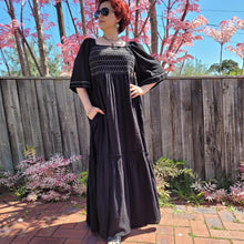 Load image into Gallery viewer, manolya-shirred-maxi-dress-with-bell-sleeves-square-neckline-empire-waist-skirt-with-ruffled-hem-in-black-outdoor-front-view-image-in-front-of-pink-tree
