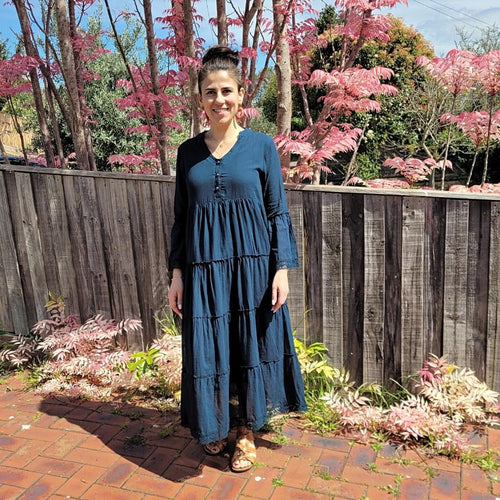 Sharon_tiered_midi_dress_in_teal_with_Vneckline_fitted_buttoned_bust_tiered_skirt_with_lace_trim_at_hem_and_bell_sleeves_with_lace_trim_front_of_pink_tree