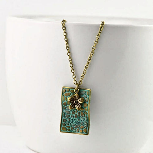 vintage-style-bronze-rectangle-pendant-necklace-with-verdigris-patina-finish-and-small-flower-charm-hanging-from-while-bowl